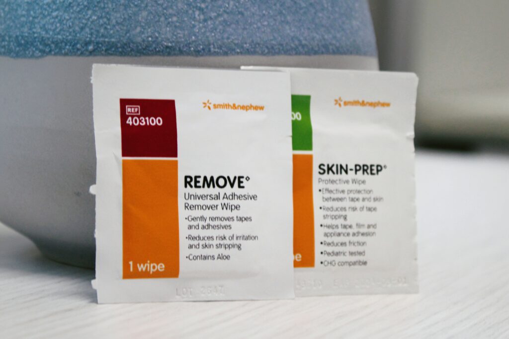 Close-up of Smith & Nephew REMOVE® adhesive remover wipe and SKIN-PREP® protective wipe sachets, designed for skin protection and safe tape removal.